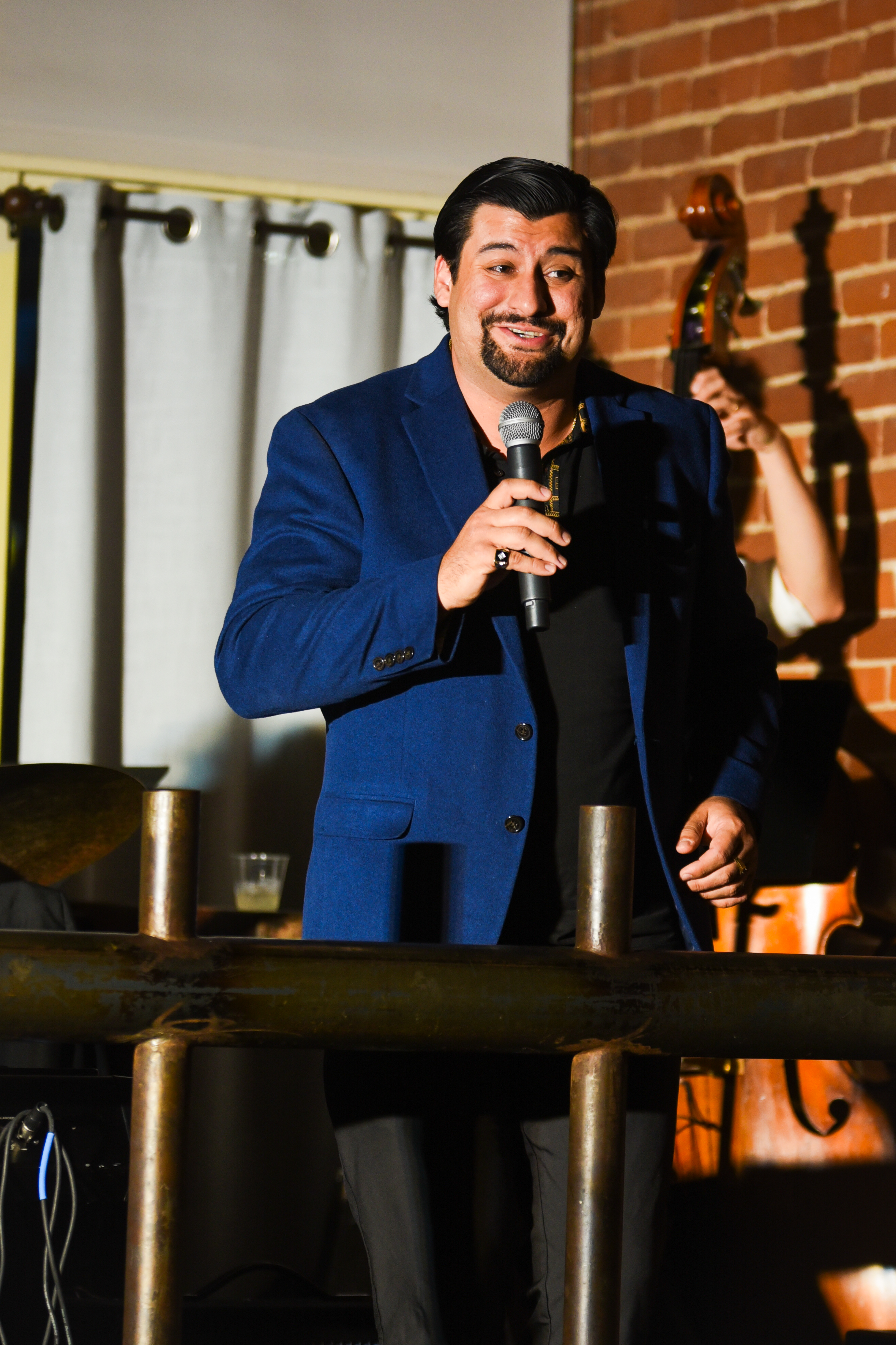 Host behind the brass railing with brick wall backdrop